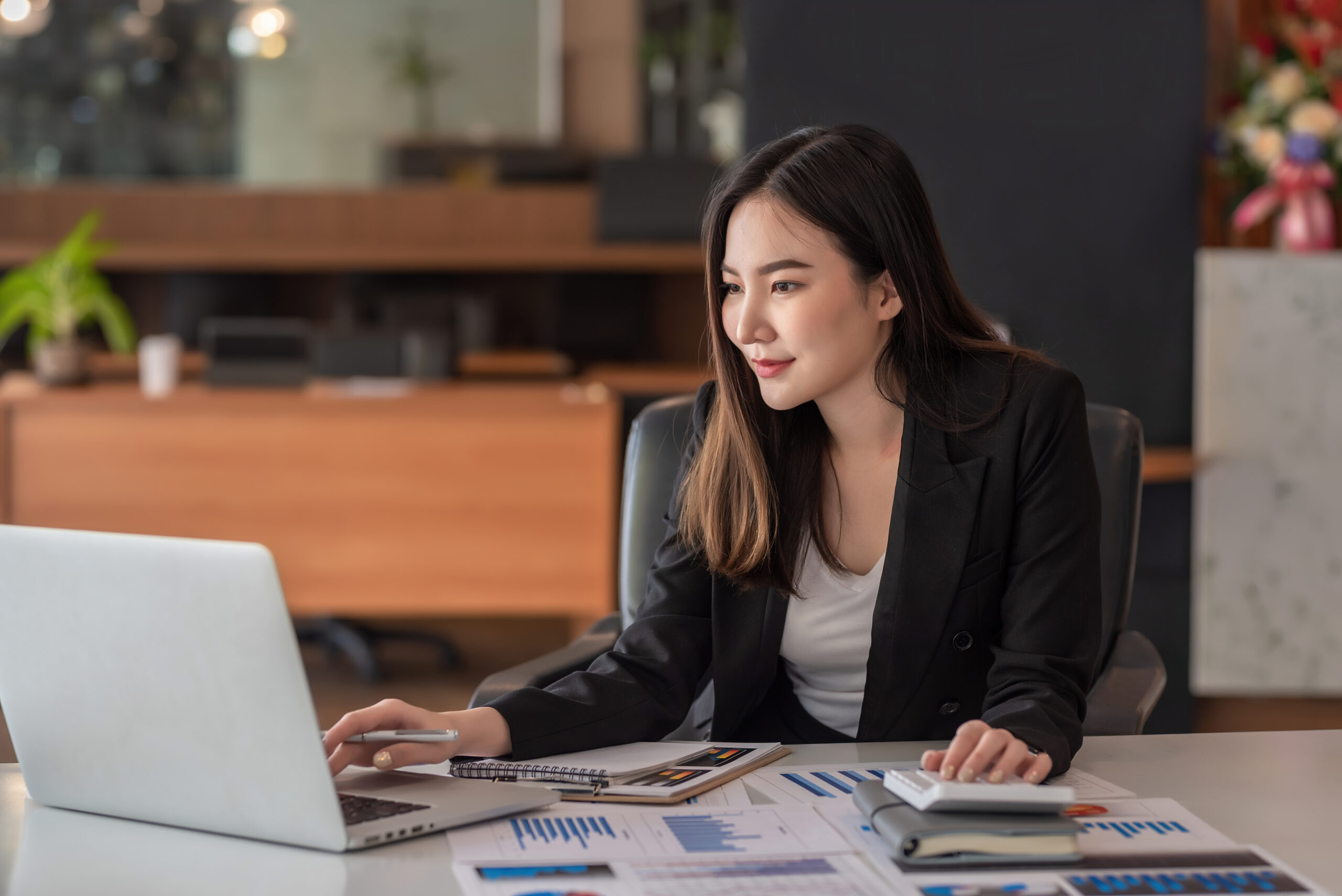 Beautiful Asian Businesswoman Analyzes Charts Using Laptop Calcu